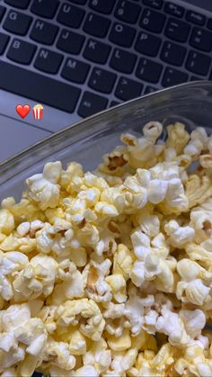 a glass bowl filled with popcorn next to a laptop