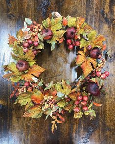 a wreath with apples, leaves and berries on it sitting on a wooden table in front of a door