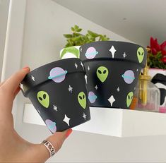 two cups with alien designs on them are being held up by someone's hand