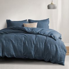 a bed with blue comforter and pillows in a room next to a lamp on the wall