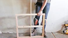 a woman standing next to a wooden shelf holding a pair of work boots in her hands