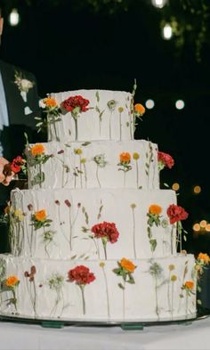 a white wedding cake with red and yellow flowers on it is being cut by a man