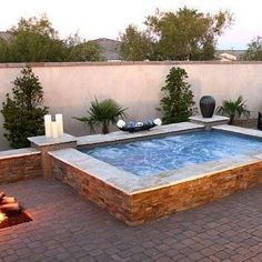 an outdoor hot tub in the middle of a brick patio with potted plants on either side