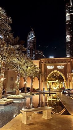 a large building with palm trees in front of it and a fountain at the entrance