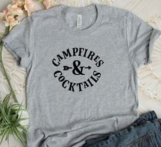 "Thanks for checking out our Campfires & Cocktails Tee! This one is perfect for all your camping trips this year!! 😊 ❤ EASY TO ORDER Select Style Shirt: Unisex Tee Select Shirt Color: Green, Dark Teal, Mauve, Gray, Black, Red, White, Blue, Army Green, Mint Select Vinyl Color: See Chart in Picture Above. Please note Vinyl Choices in the \"nites to seller\" when checking out. If no vinyl choice is written, shirt will be sent exactly as pictured in the first picture. ❤ SHIRT SPECIFICATIONS &am Mrs Shirt, Mountain Shirt, Women Camping, Adventure Shirt, Travel Shirts, Camping Shirt, Summer Tshirts, Unisex Shirts, Campfire