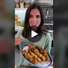 a woman holding a plate with chicken skewers on it and pointing to the camera