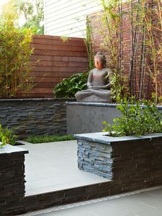 a buddha statue sitting on top of a stone block wall next to a planter filled with plants