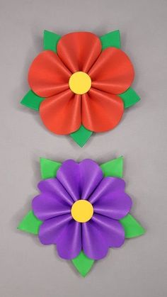 two paper flowers with green stems and orange centers, one purple and one red flower