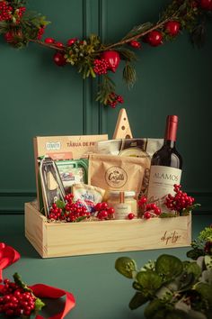 a wooden box filled with wine, cheese and other holiday foods next to holly wreath