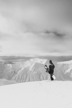 a man standing on top of a snow covered slope holding a snowboard in his hand