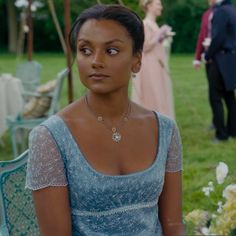 a woman in a blue dress is sitting on a chair and looking at the camera