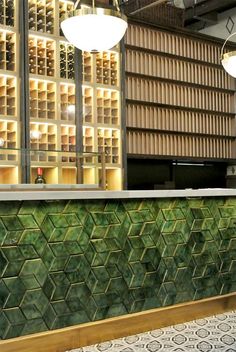 a green tiled counter in front of a wine rack with bottles on it and lights hanging from the ceiling