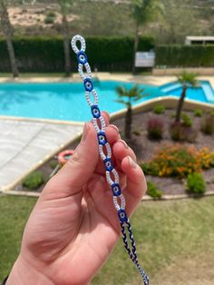 a person holding up a blue and white beaded necklace in front of a swimming pool