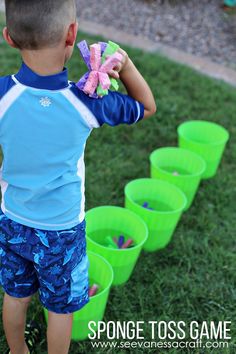 a young boy standing in front of green buckets with pink and blue items on them