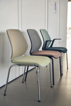 four different colored chairs are lined up against the wall in an empty room with white walls