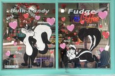 two windows decorated with black and white cats in front of storefronts that have hearts hanging from them