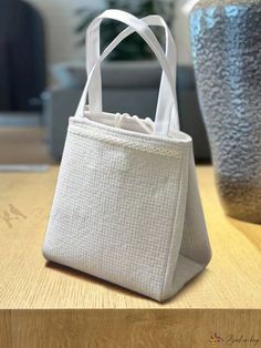 a white tote bag sitting on top of a wooden table next to a vase