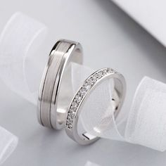 two white gold wedding bands with diamonds on them, sitting next to each other in front of a white cloth