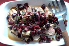 a white plate topped with meat covered in cranberry sauce and garnished with cherries