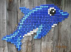 a blue and white fish made out of plastic bottle caps on a wooden fence post