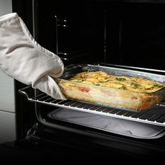 a person is taking a casserole out of the oven with their gloved hand