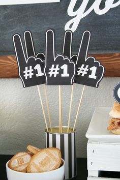 a table topped with sandwiches and cupcakes on top of a white plate next to a black and white sign