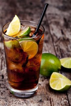 a glass filled with ice and limes on top of a wooden table