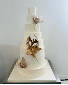 a three tiered white wedding cake with gold leaves on the top and bottom layer