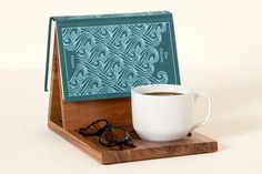 a cup of coffee sitting on top of a wooden coaster next to a pair of glasses