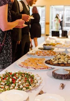 people are standing around a buffet table with food on plates and serving utensils