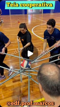 three men are playing with a ball on an indoor basketball court while another man watches from the sidelines