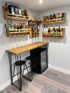 a bar with two stools next to it and shelves filled with wine glasses on the wall