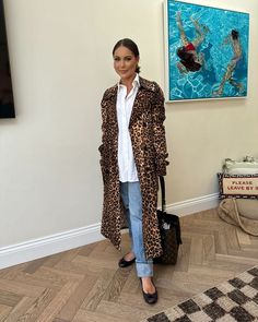 a woman standing in front of a painting and holding a black bag while wearing a leopard print coat