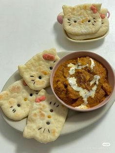 a white plate topped with crackers next to a bowl filled with cat shaped food