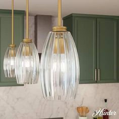 two clear glass pendant lights hanging from a kitchen ceiling over a counter top with green cabinets