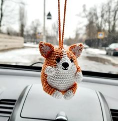 a crocheted dog hanging from the dashboard of a car with snow on the ground