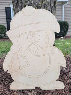 a wooden cutout of a snowman sitting in front of a tree