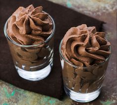 two glasses filled with chocolate frosting on top of a table