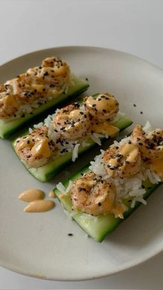 three pieces of cucumber with shrimp and rice on top, garnished with sesame seeds