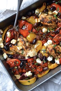 a pan filled with chicken and vegetables on top of a white table cloth next to a fork