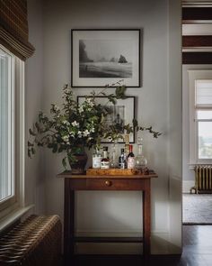 a wooden table topped with lots of bottles and vases next to a painting on the wall