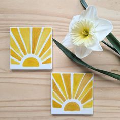 two yellow and white coasters sitting on top of a wooden table next to a flower