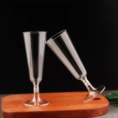 two glasses sitting on top of a wooden cutting board next to each other with leaves in the background