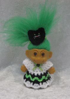 a small doll with green hair and a black cat on it's head, wearing a dress