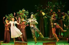 a group of people standing on top of a stage in front of trees and flowers