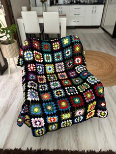 a multicolored crocheted afghan sits on the floor in front of a dining room table