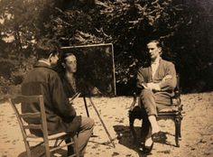 two men sitting on chairs in front of an easel and another man standing next to them