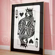 a framed playing card with the queen of spades on it in front of a pink wall