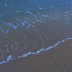 the ocean waves are coming in and out of the water at the beach with blue foam on the sand