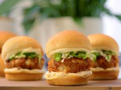 three small sandwiches with meat and lettuce on them sitting on a wooden table